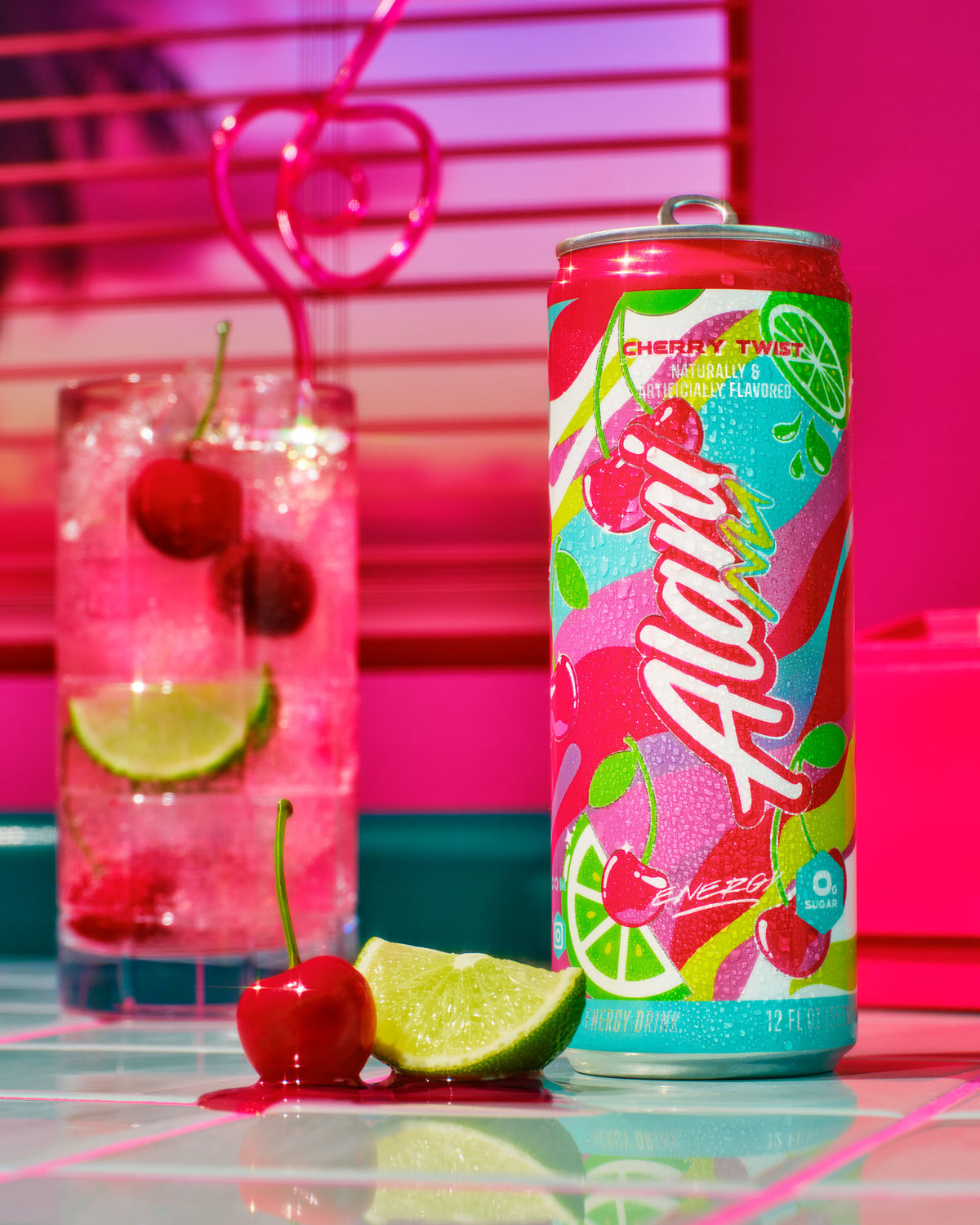 A can of Cherry Twist energy drink is flanked by a cherry-decorated glass of pink soda and fresh lime and cherry on a reflective surface.