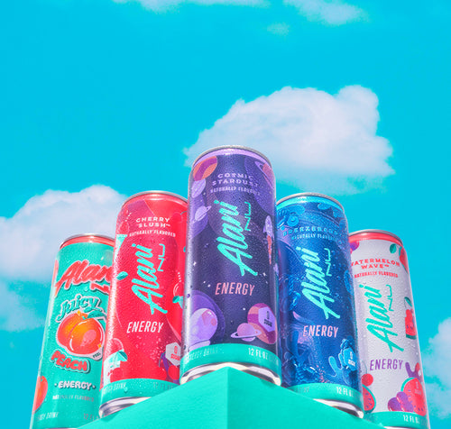 Five sugar-free Alani Energy Drink cans on a seafoam shelf in front of a blue sky.