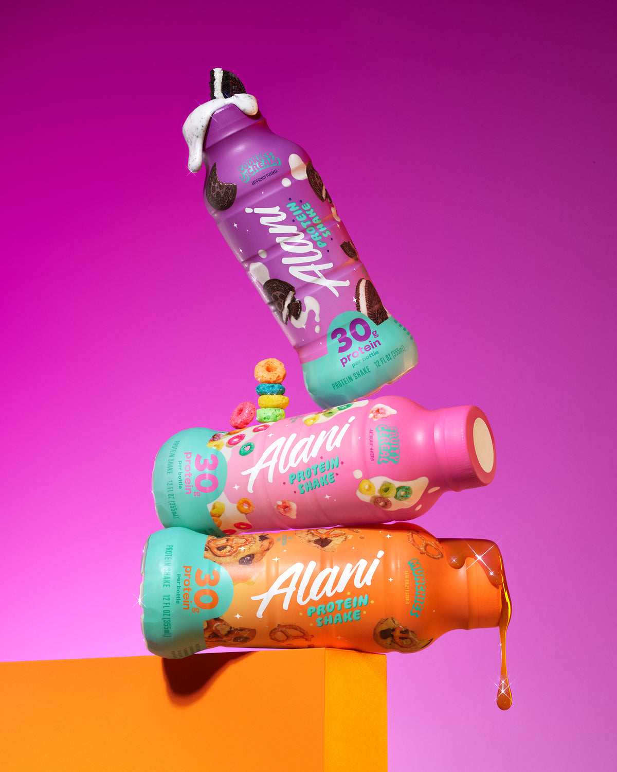 A trio of Alani Nu 30-gram protein shakes: Cookies & Cream, Fruity Cereal, and Munchies, stacked on an orange ledge against a purple gradient background.
