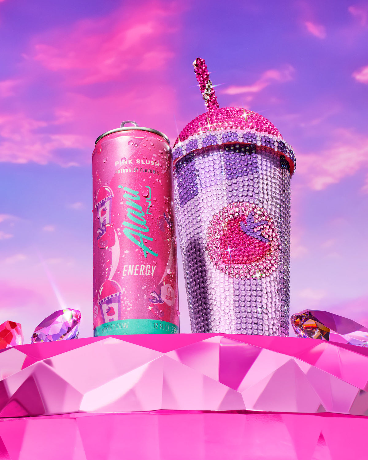 Alani Nu Pink Slush Energy Drink can next to a purple and pink bedazzled slushie cup.  