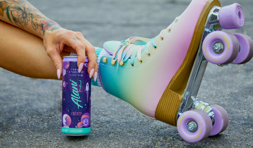 A girl hand holding an Alani Nu Energy Drink with roller blades on.