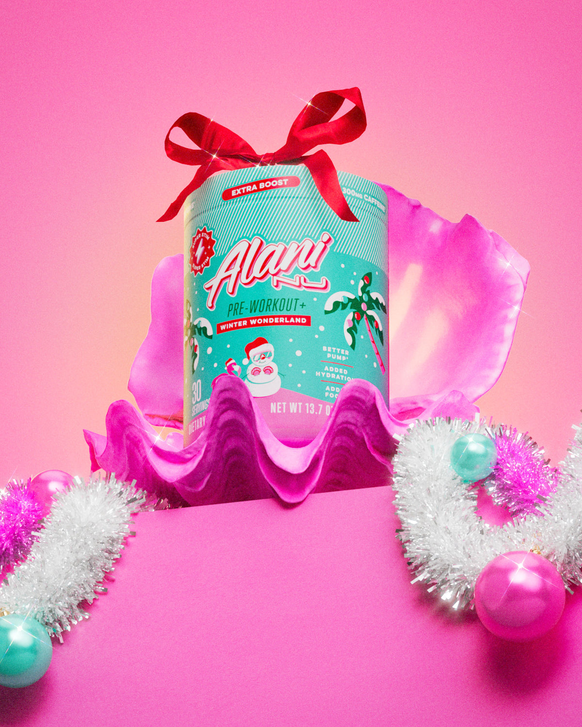 A tub of Alani Nu's limited-edition Winter Wonderland Pre-Workout+ glowing in a pink clamshell decorated with ornaments, ribbon, and tinsel.