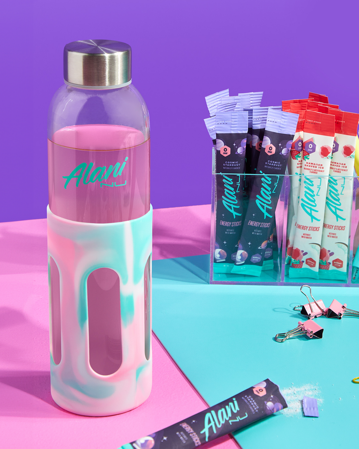 A pink marble glass water bottle next to an Alani Energy Sticks. 