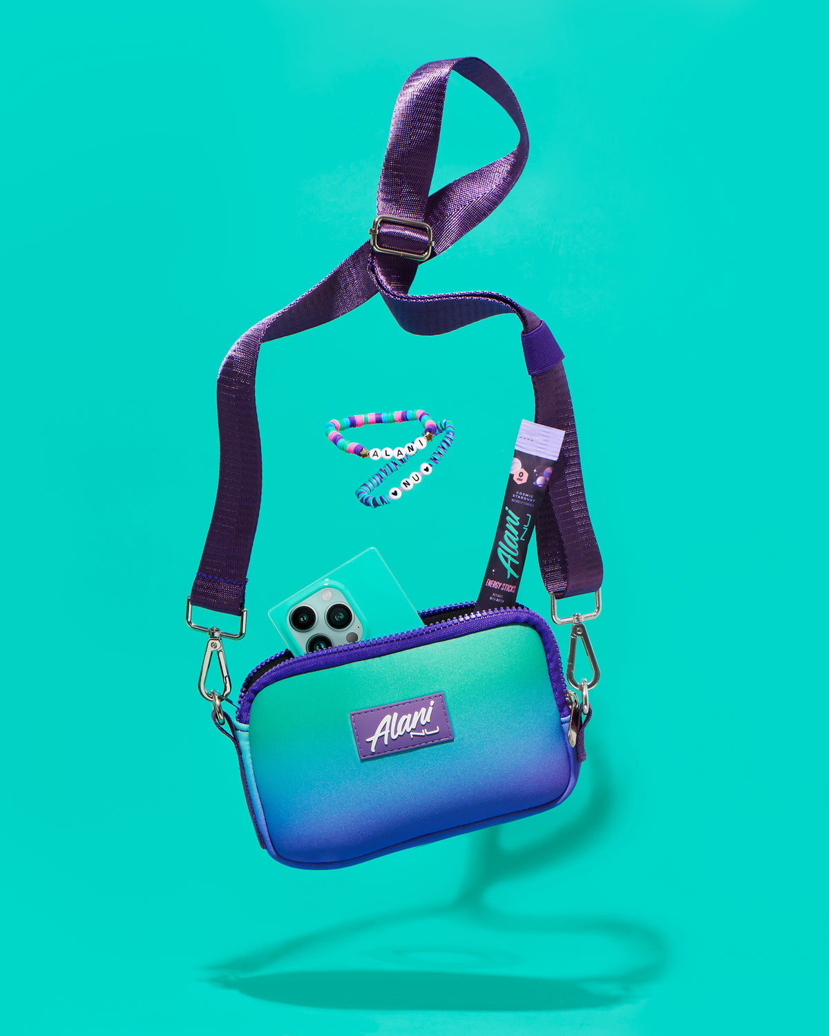 A shoulder bag in twilight sky color displayed with energy stick breezeberry flavor and an Iphone. 