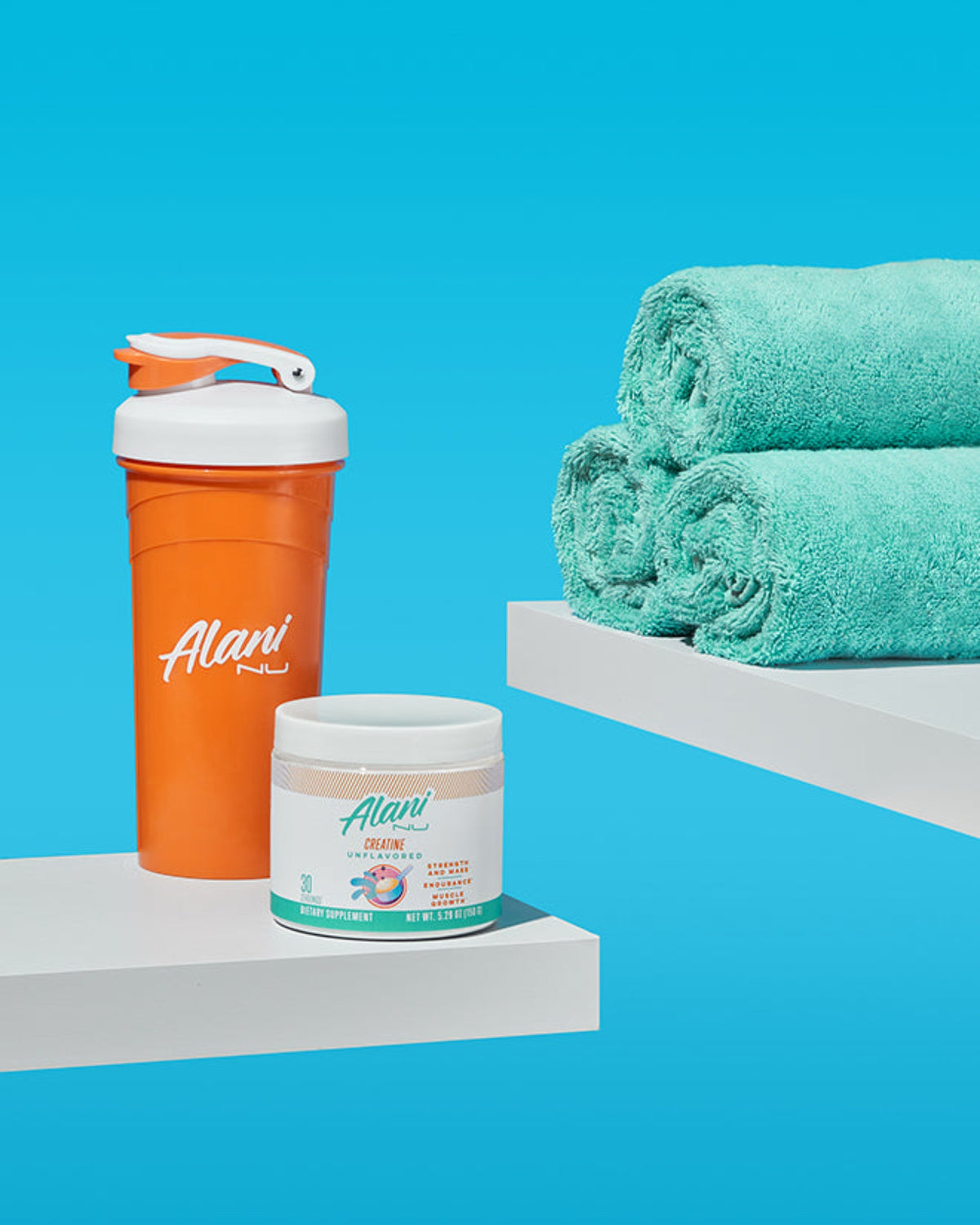 A Alani Nu Shaker sitting next to a Creatine container by a stack of towels. 