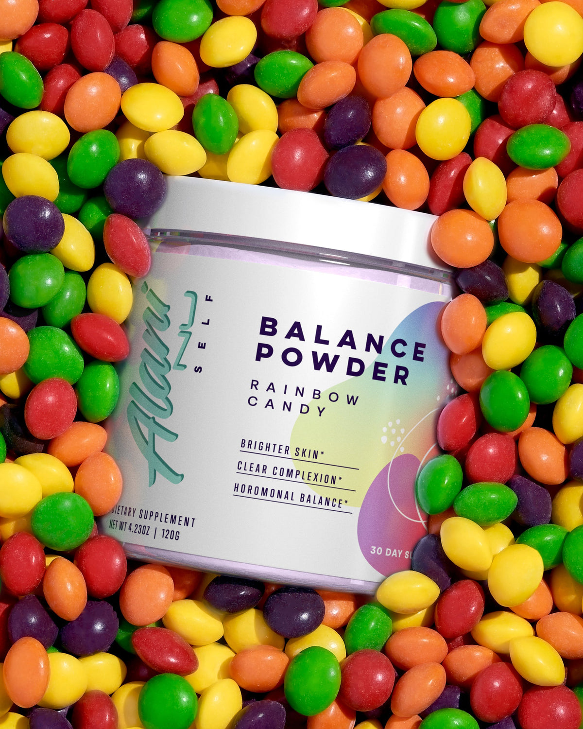 A container of Balance Powder in Rainbow Candy sitting  flavor on a pile of candy.