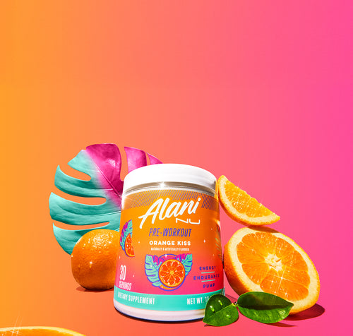 A tub of Orange Kiss Alani Nu Pre-Workout surrounded by orange slices and a palm leaf.