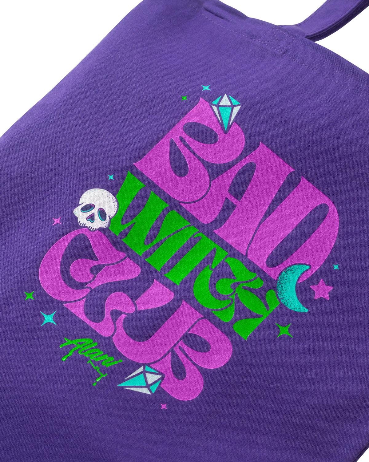 A close up detail shot of Witch&#39;s Brew Tote bag with purple and green logo stating bad witch club.