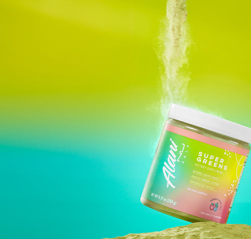A tub of Alani Nu Peach Iced Tea Super Greens on a pile of vitamin-rich powder. 