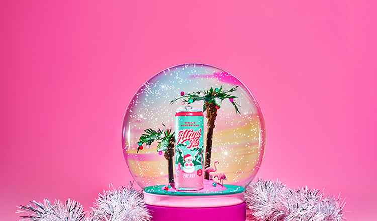 Alani Nu's limited-edition Winter Wonderland Energy inside a tropical snow globe. Faux flurries fall on paper palm trees and flamingo figurines. 