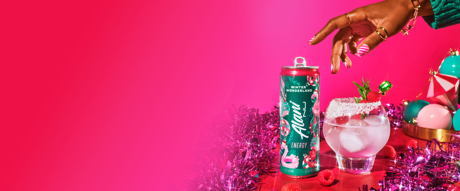 Alani Nu Winter Wonderland Energy Drink sits next to a frosty glass garnished with raspberries and holiday decorations, against a vibrant pink festive backdrop.