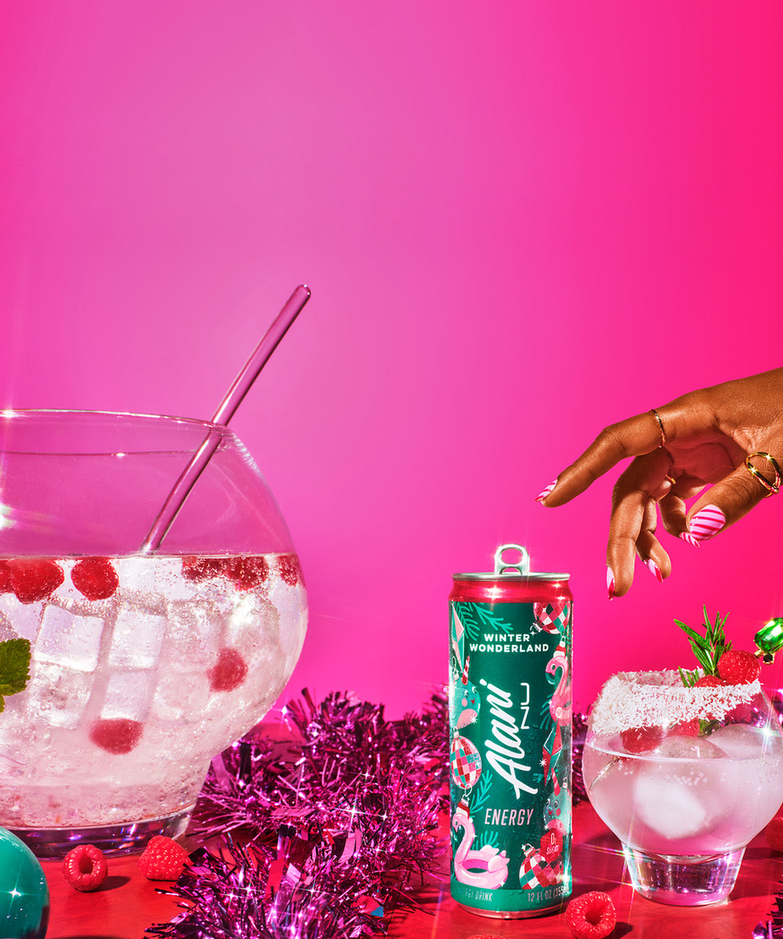 Alani Nu Winter Wonderland Energy Drink sits next to a frosty glass garnished with raspberries and holiday decorations, against a vibrant pink festive backdrop.