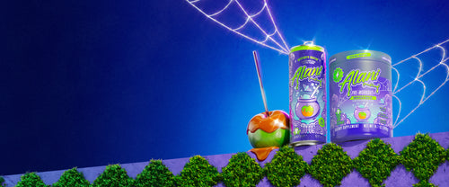 A caramel apple leaning on Alani Nu's fall Witch's Brew Energy Drink and Pre-Workout+ atop a mossy garden wall. Bejeweled cobwebs fill the frame.
