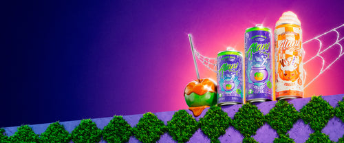 A caramel apple with Alani Nu’s 3 limited-edition fall Energy Drinks—Mini Witch’s Brew, Witch’s Brew, and new Pumpkin Cream—on a garden ledge.
