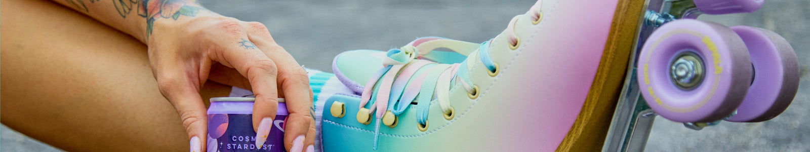 A girl hand holding an Alani Nu Energy Drink with roller blades on.