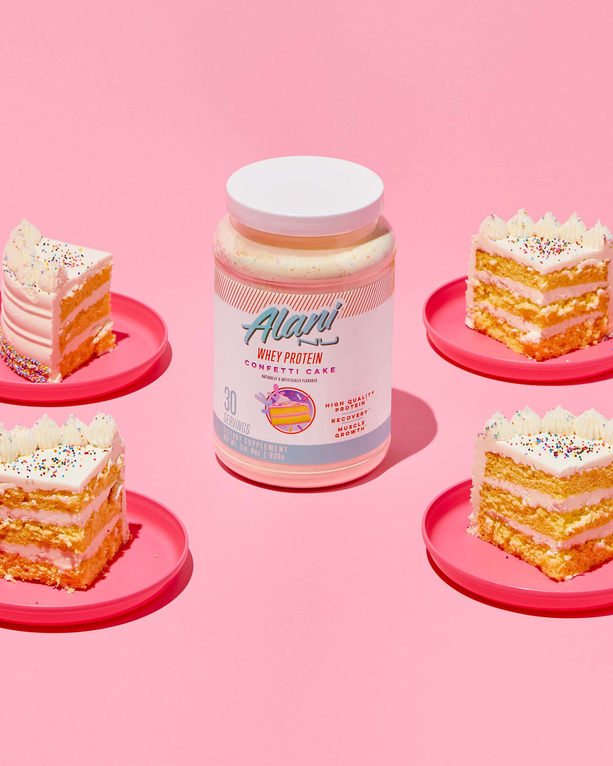 A pink plate topped with a piece of Alani Nu Cake next to a container of Whey Protein - Confetti Cake.