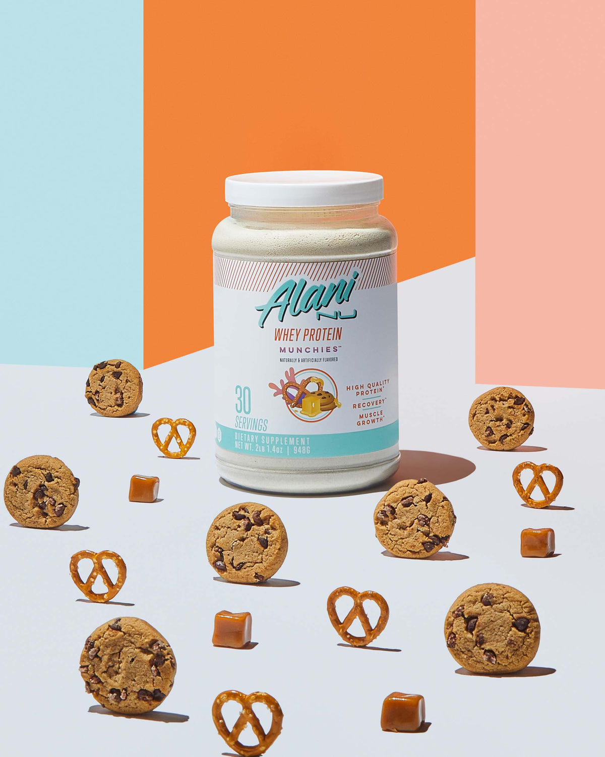 A container  of Whey Protein - Munchies by Alani Nu surrounded by cookies and pretzels.