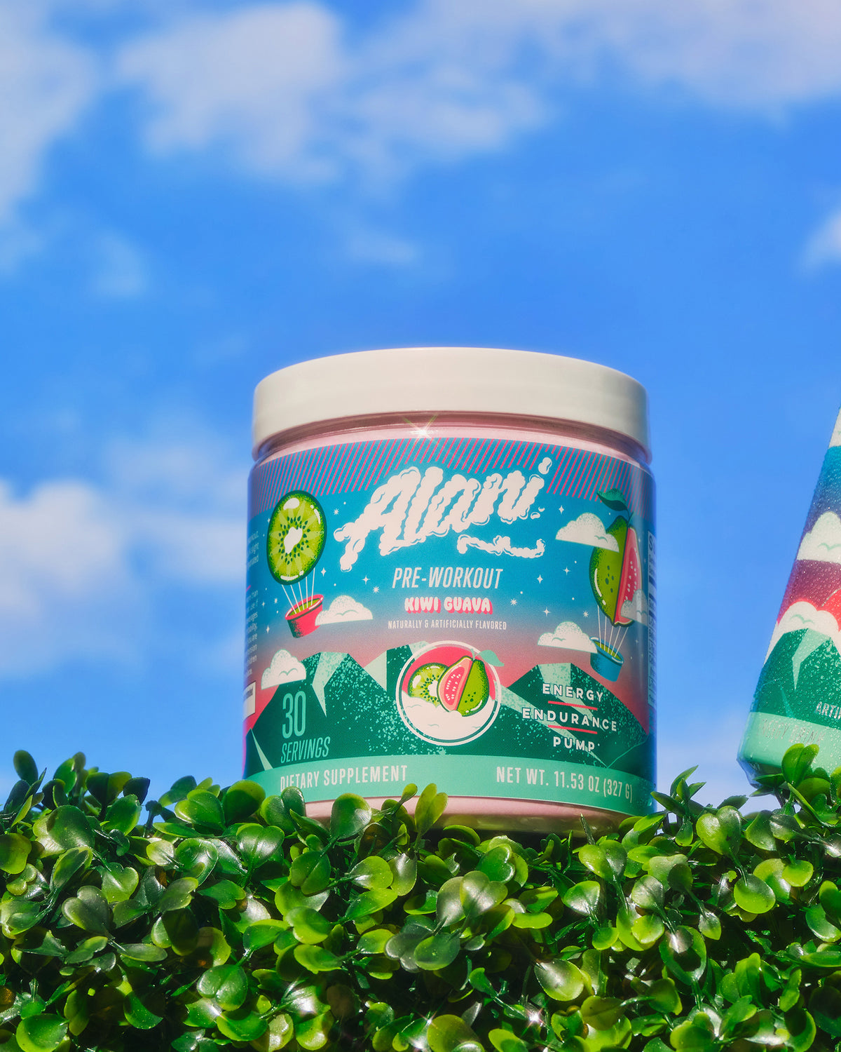 A container of Alani Nu Pre- Workout Kiwi Guava sitting on top of a bush.