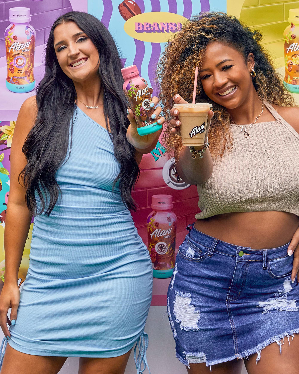 Two women standing next to each other holding Alani Nu Mocha coffees.