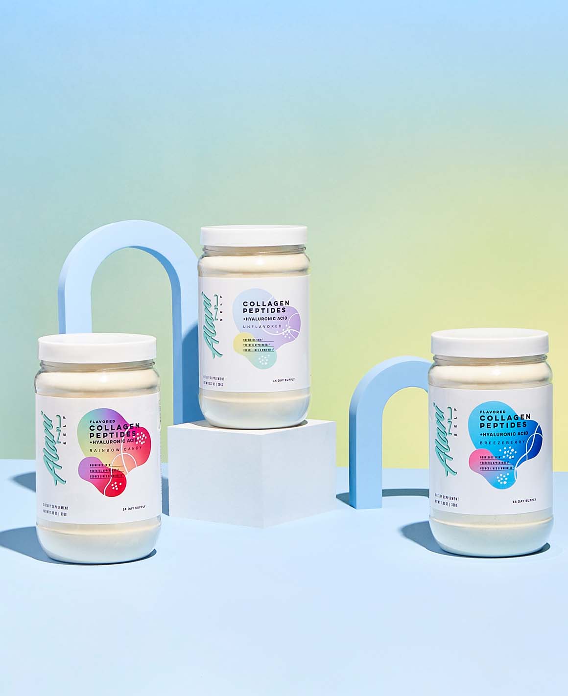 Three 14-day containers of Alani Nu Collagen Peptides - Unflavored, Rainbow Candy &amp; Breezeberry sitting on a table.