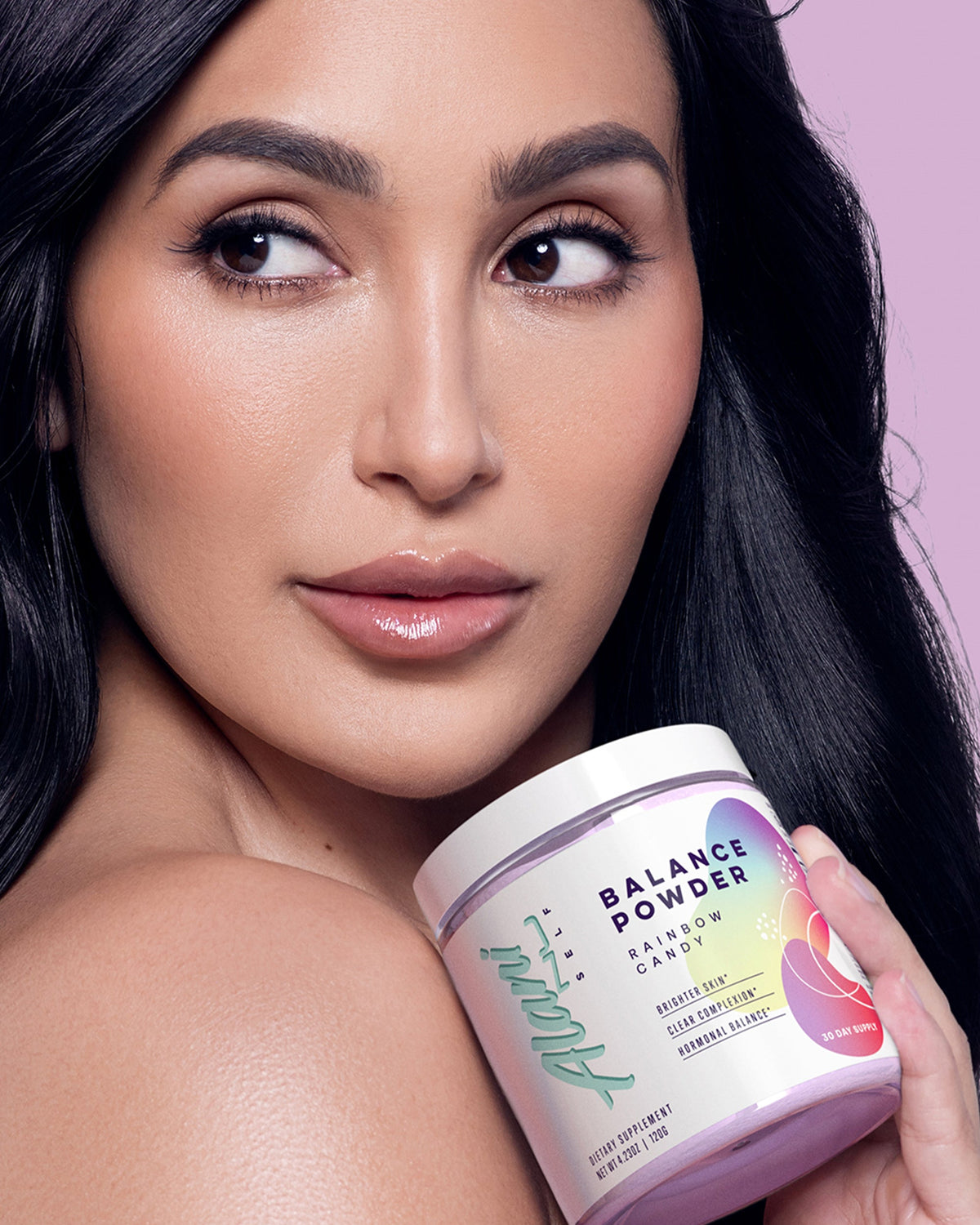A woman holding a container of Alani Nu Balance Powder in Rainbow Candy flavor.